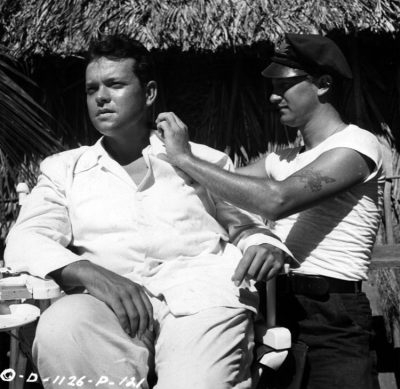 <a href="https://www.aenigma-images.com/d-1126-p-121-cronenweth-welles-schiffer-shanghai-behind-the-scenes/">More information.</a> Orson Welles gets a quick trim from makeup expert Bob Schiffer between scenes of The Lady from Shanghai